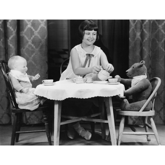 black and white image of a girl having a tea party with her dolly and teddy bear