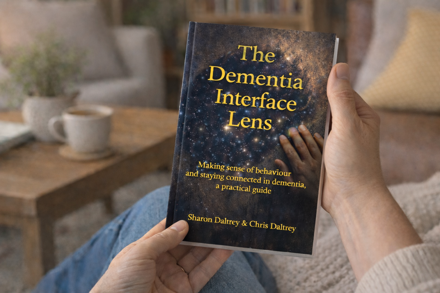 Person holding a book titled 'The Dementia Interface Lens' in a cozy indoor setting.