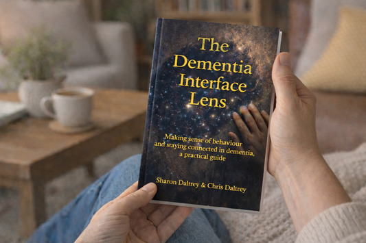 Person holding a book titled 'The Dementia Interface Lens' in a cozy indoor setting.